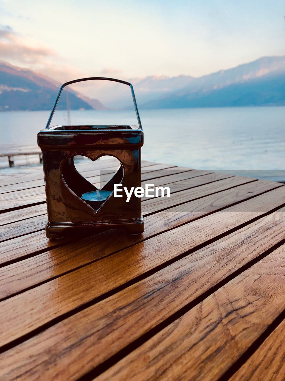 Tea light in lantern on pier over lake against sky