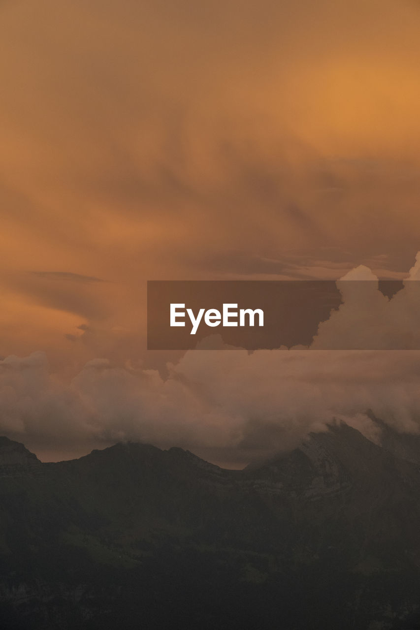 Scenic view of mountains against cloudy sky at sunset