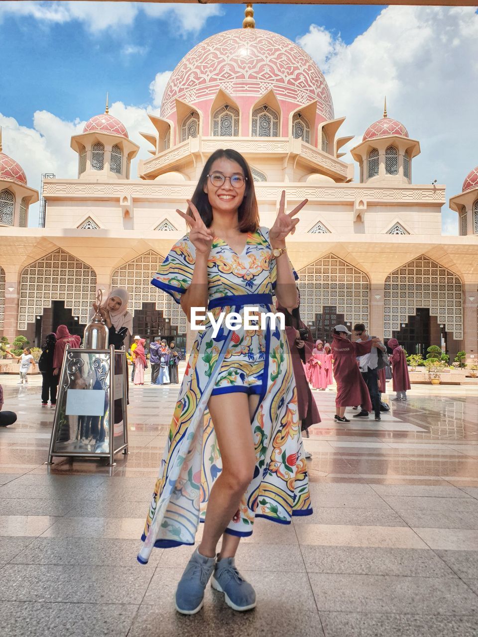 Full length portrait of smiling young woman showing peace signs outside historic building