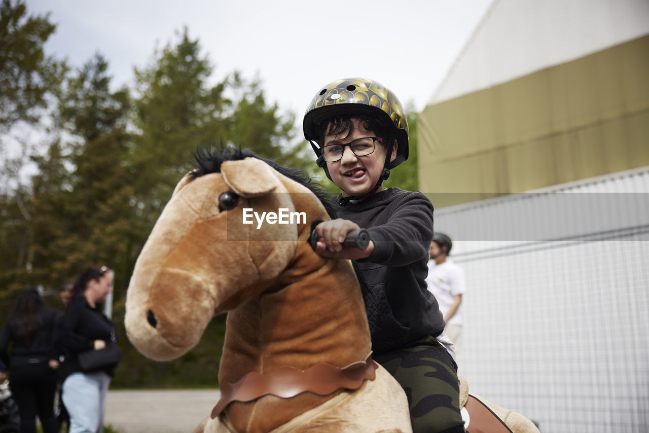 Portrait of boy having fun riding horse on wheels outdoors