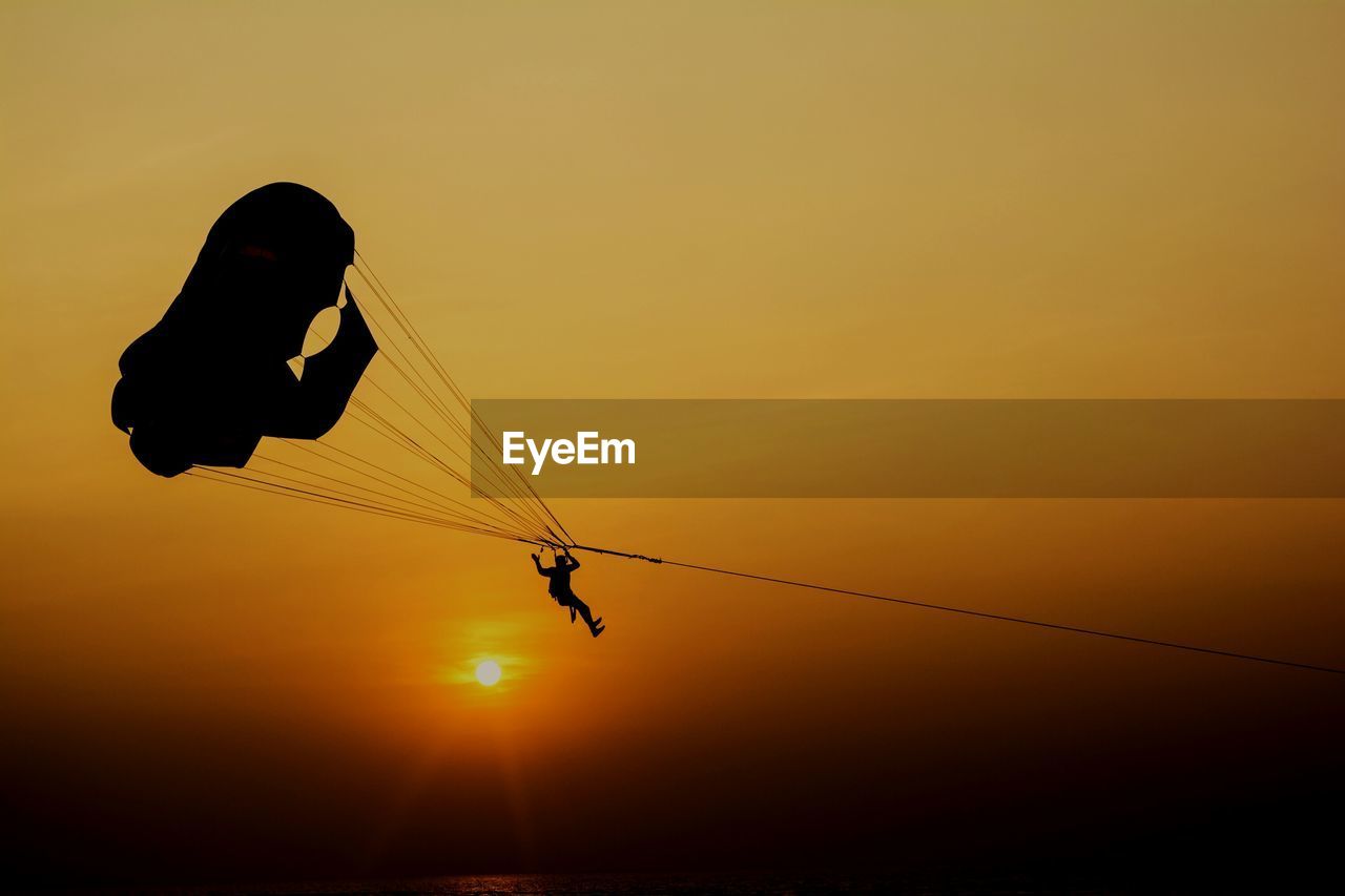 Silhouette person paragliding against clear sky during sunset