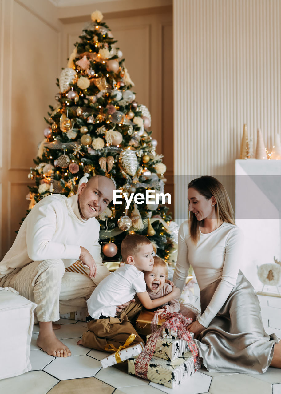 A family with children celebrate give gift boxes decorate a christmas tree in the interior the house