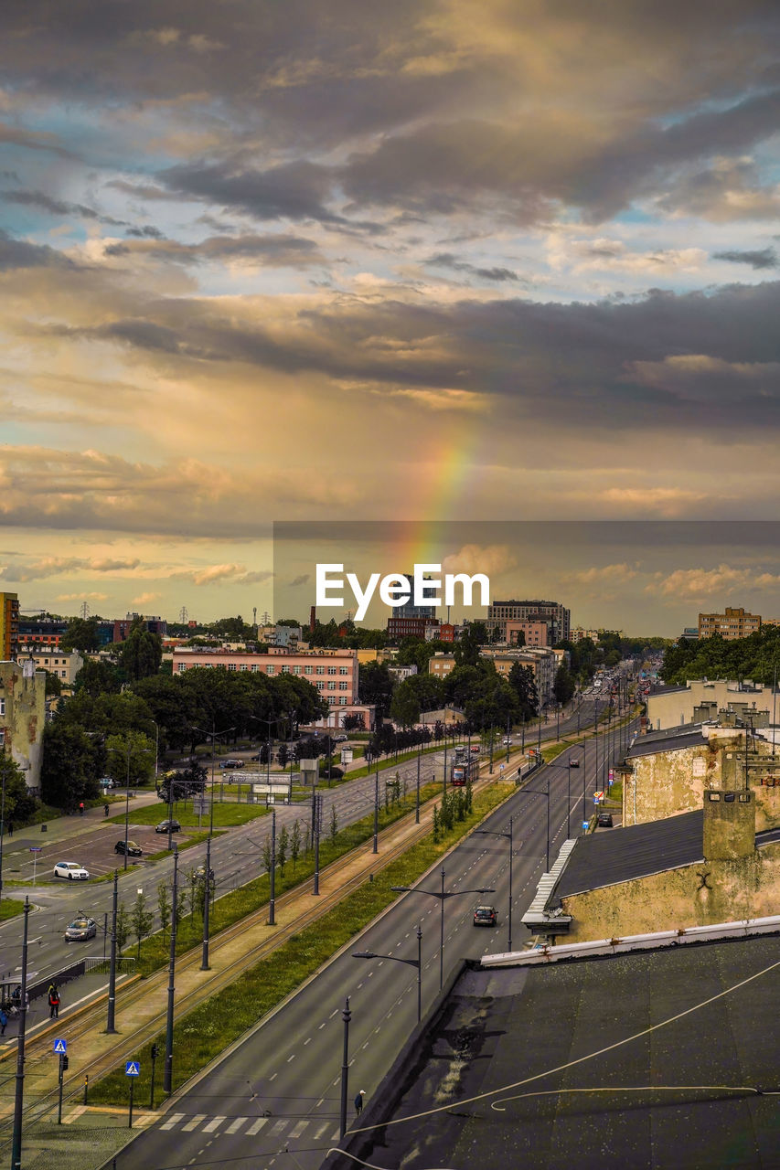 Cityscape with mix of modern and medieval architecture next to highway against sky and rainbow