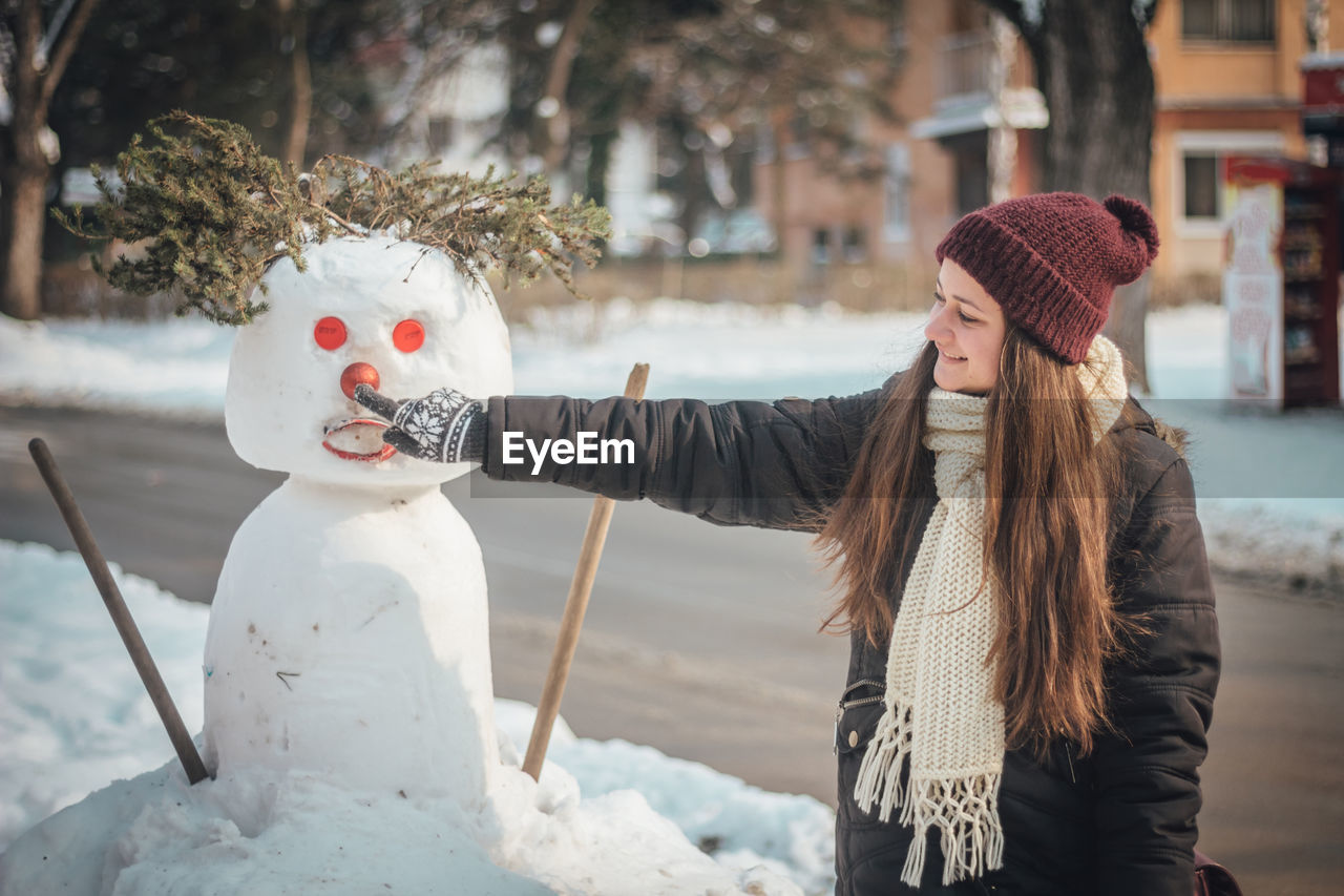 Smiling woman touching snowman in city