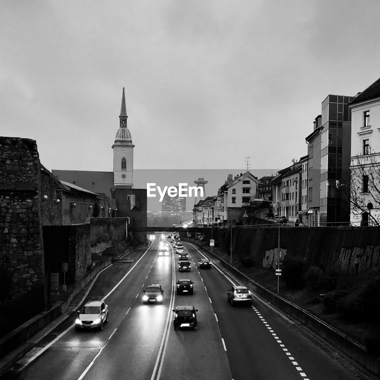 VEHICLES ON ROAD AMIDST BUILDINGS AGAINST SKY