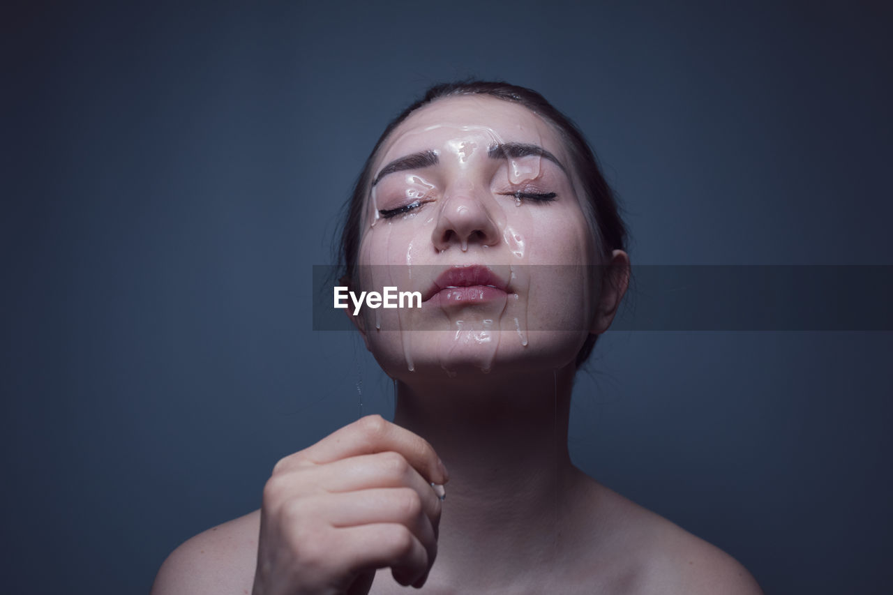 Close-up of shirtless young woman with beauty product on face against gray background