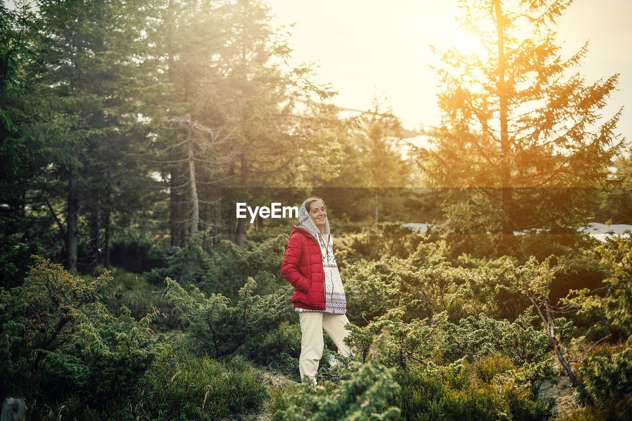 Portrait of smiling woman wearing warm clothing standing amidst plants in forest