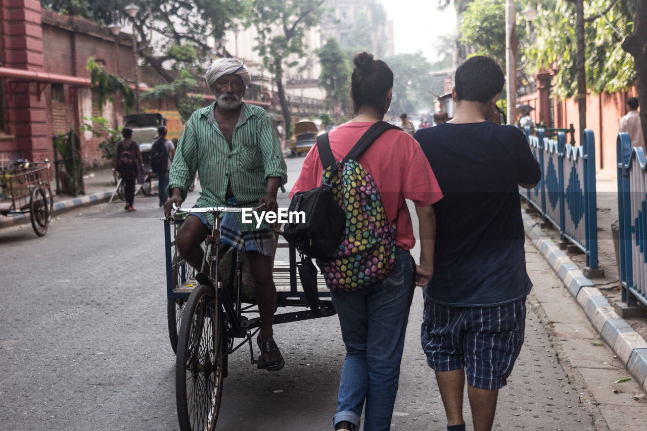 Rear view of couple walking by senior man riding pedicab on street