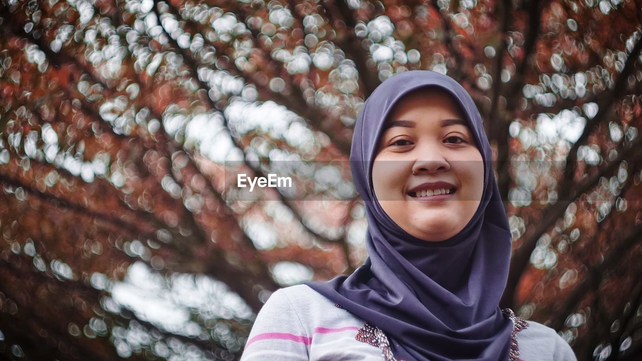 Portrait of smiling woman against tree