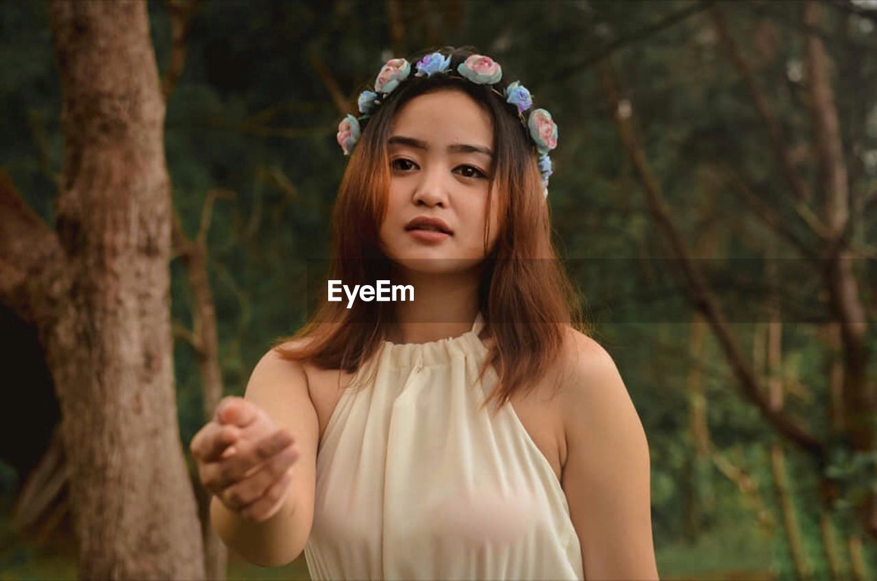 Portrait of beautiful young woman gesturing against trees in forest