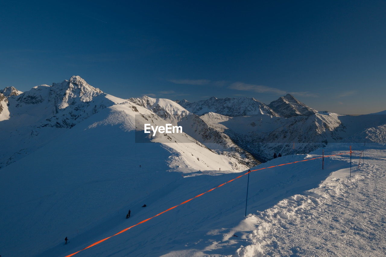 snow, winter, cold temperature, mountain, mountain range, scenics - nature, environment, beauty in nature, landscape, nature, snowcapped mountain, piste, ski mountaineering, sky, winter sports, skiing, ski touring, sports, travel, travel destinations, day, ski, ski equipment, blue, tranquility, white, tranquil scene, outdoors, non-urban scene, mountain peak, sunlight, tourism, ridge, vacation, land, transportation