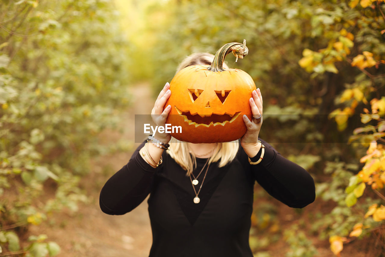 MIDSECTION OF WOMAN HOLDING PUMPKIN DURING HALLOWEEN