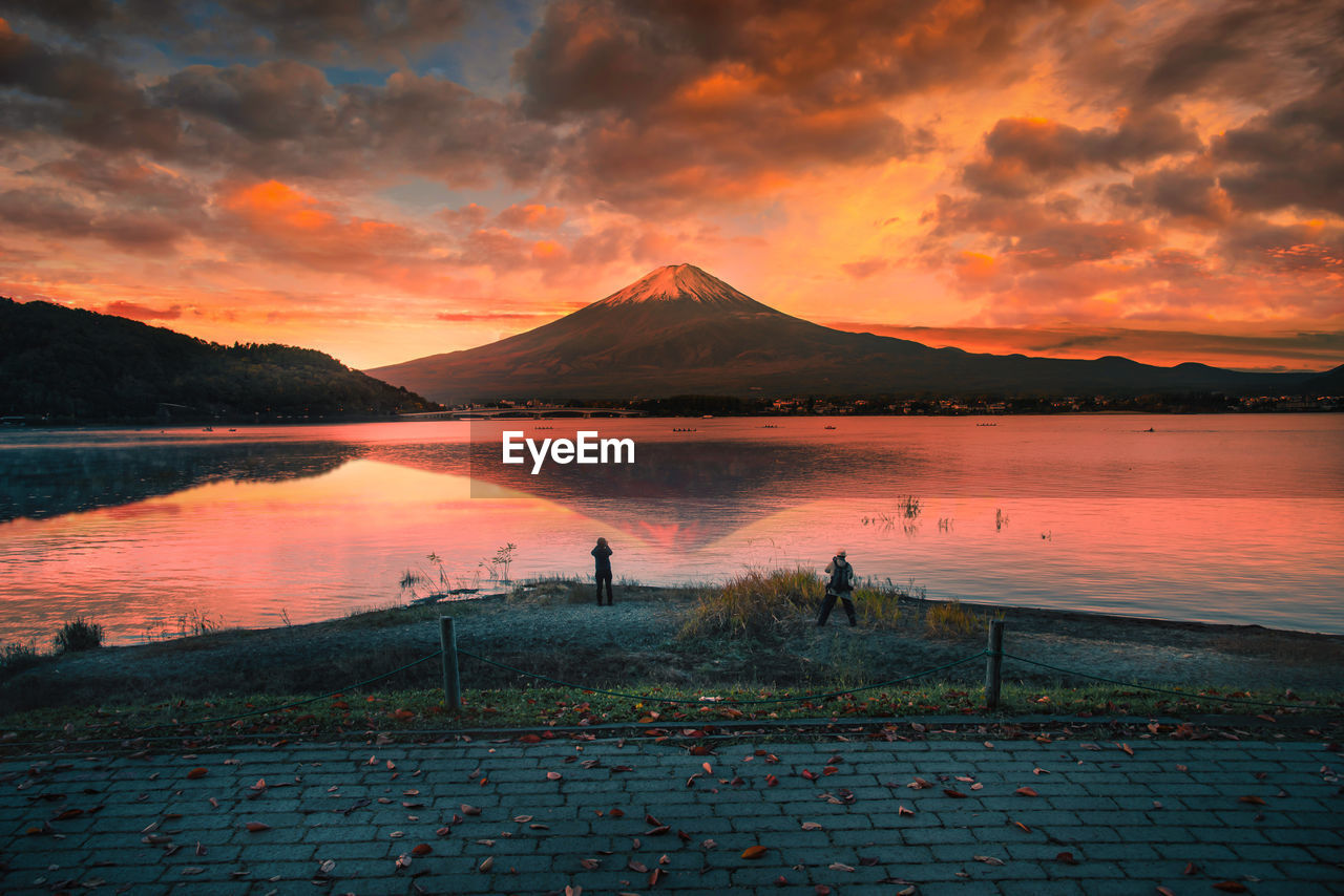 Rear view of men standing by lake against sky