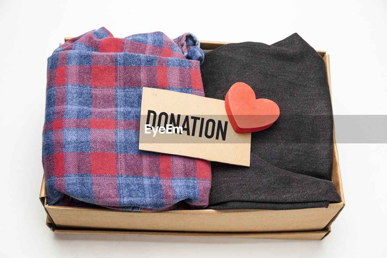 High angle view of clothing with heart shape in donation box over white background