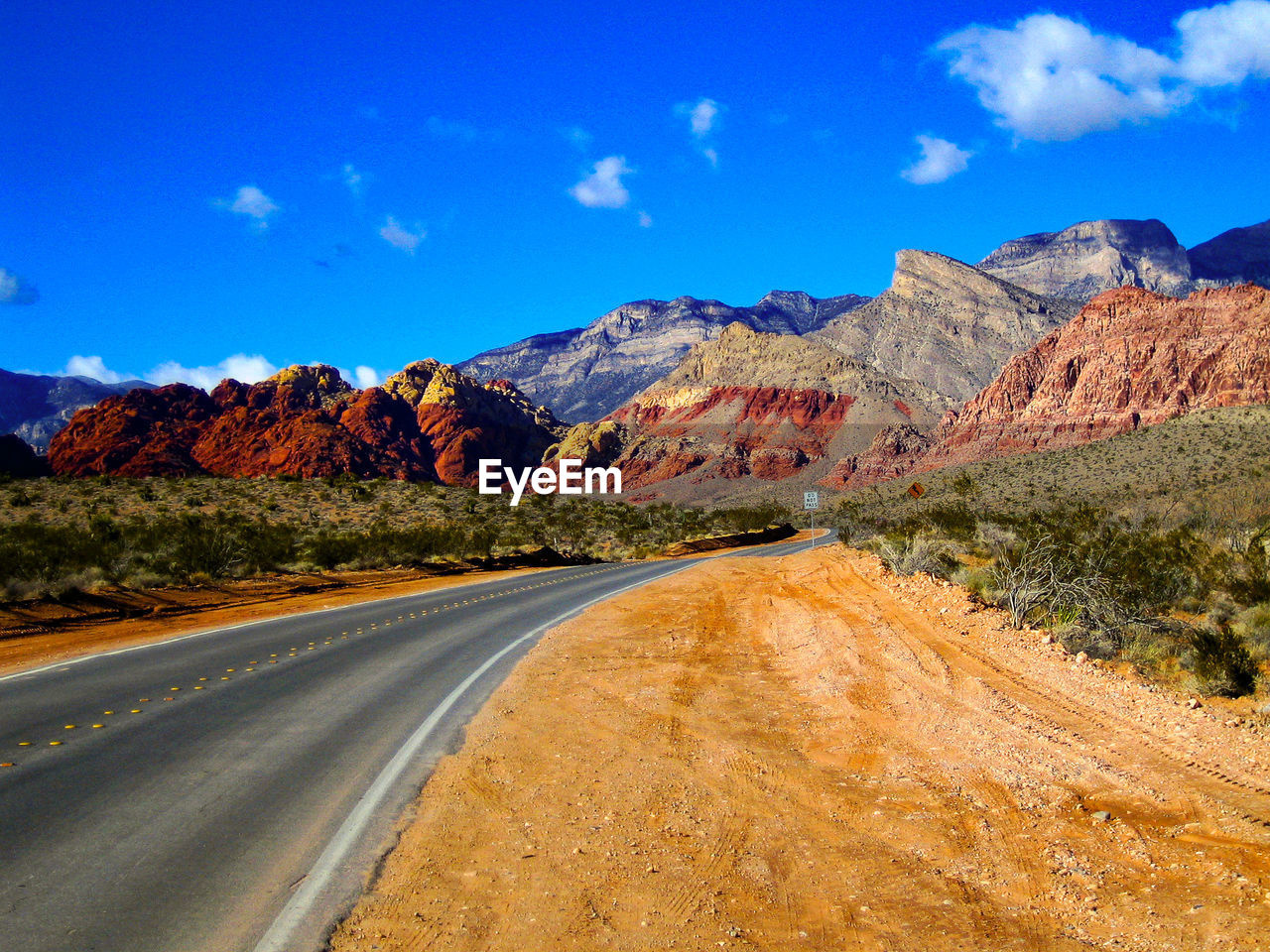 Road leading towards mountains against blue sky