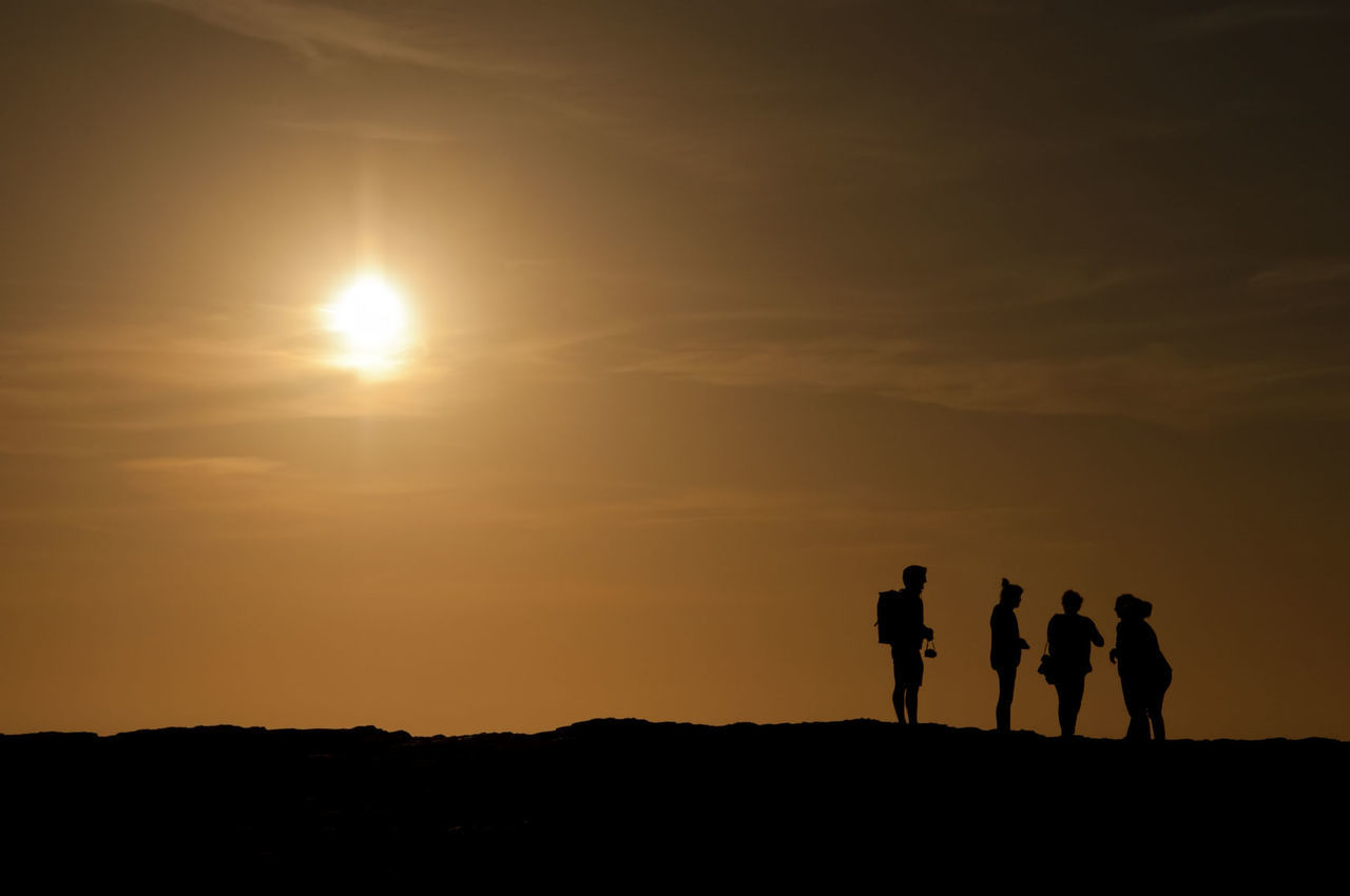 Silhouette friends on mountain against sky during sunset