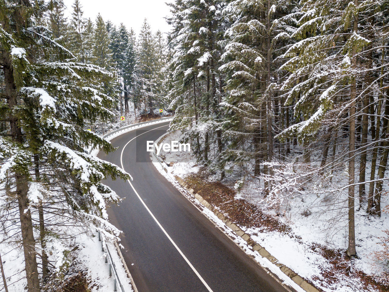 Curvy windy road in snow covered forest, top down aerial view