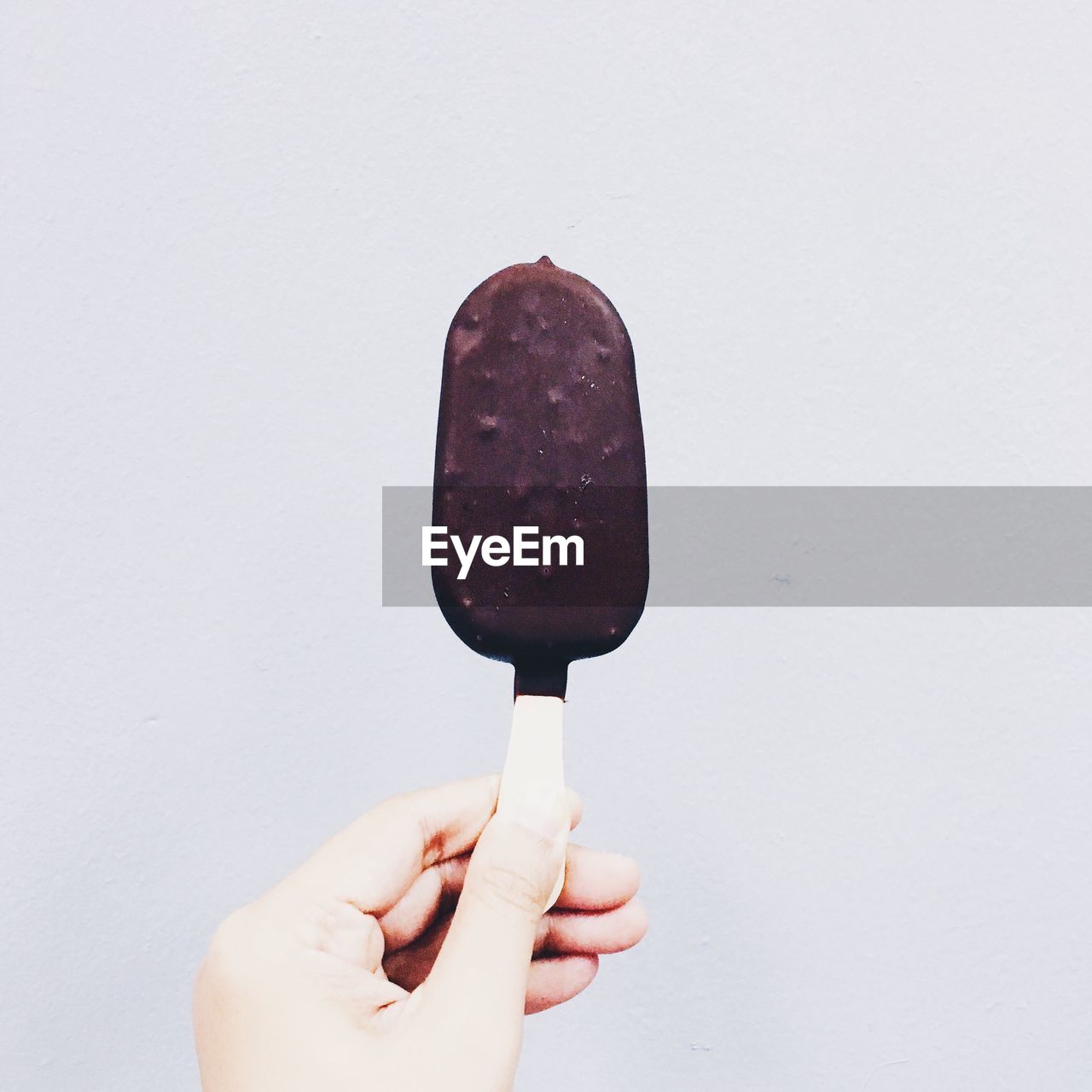 Cropped hand holding chocolate covered ice cream against white background