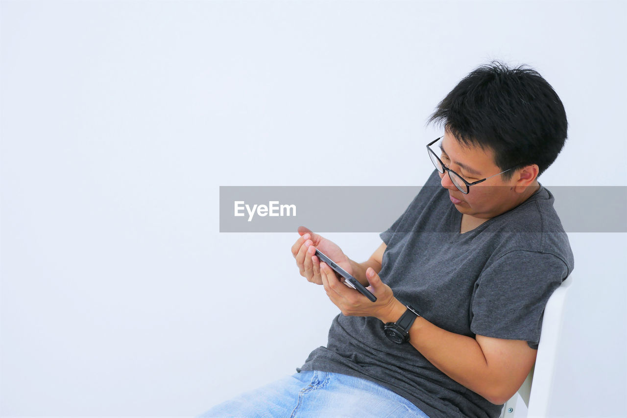 Mature man using smart phone while sitting on chair against white background