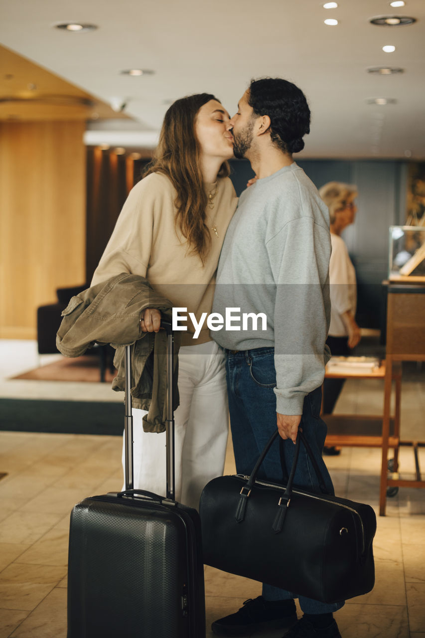 Couple with luggage kissing while standing in hotel lobby