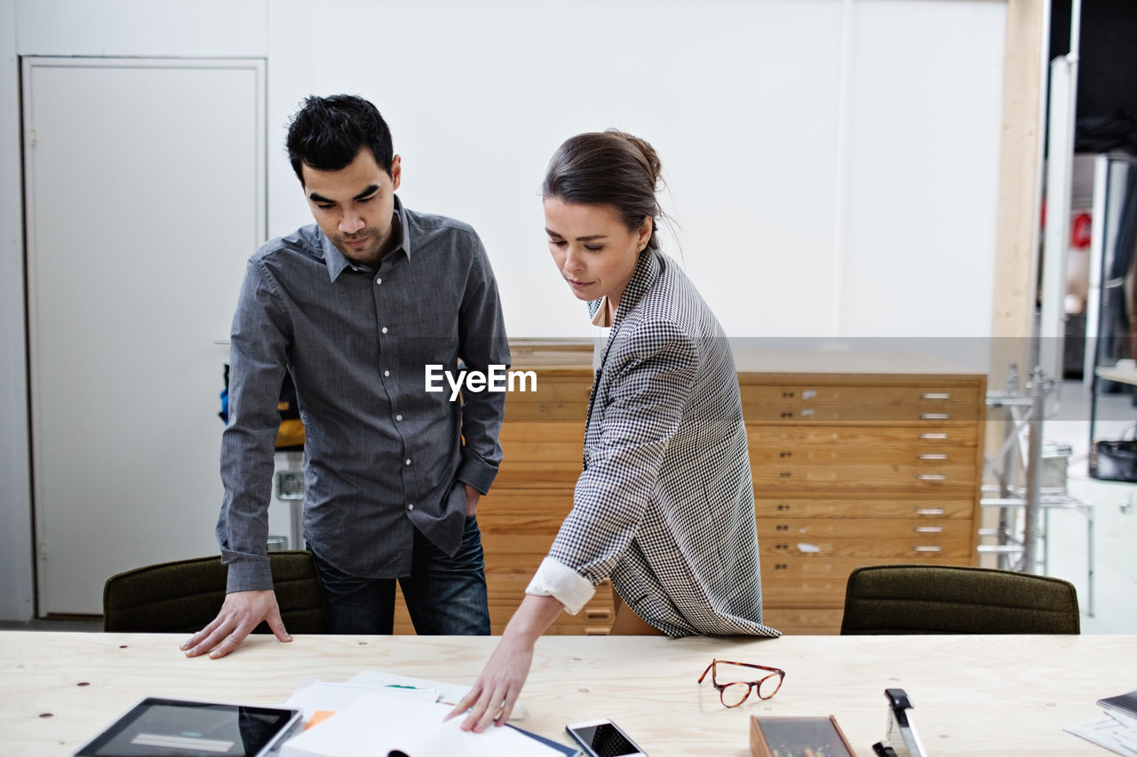 Confident male and female business colleagues discussing over documents at table in office