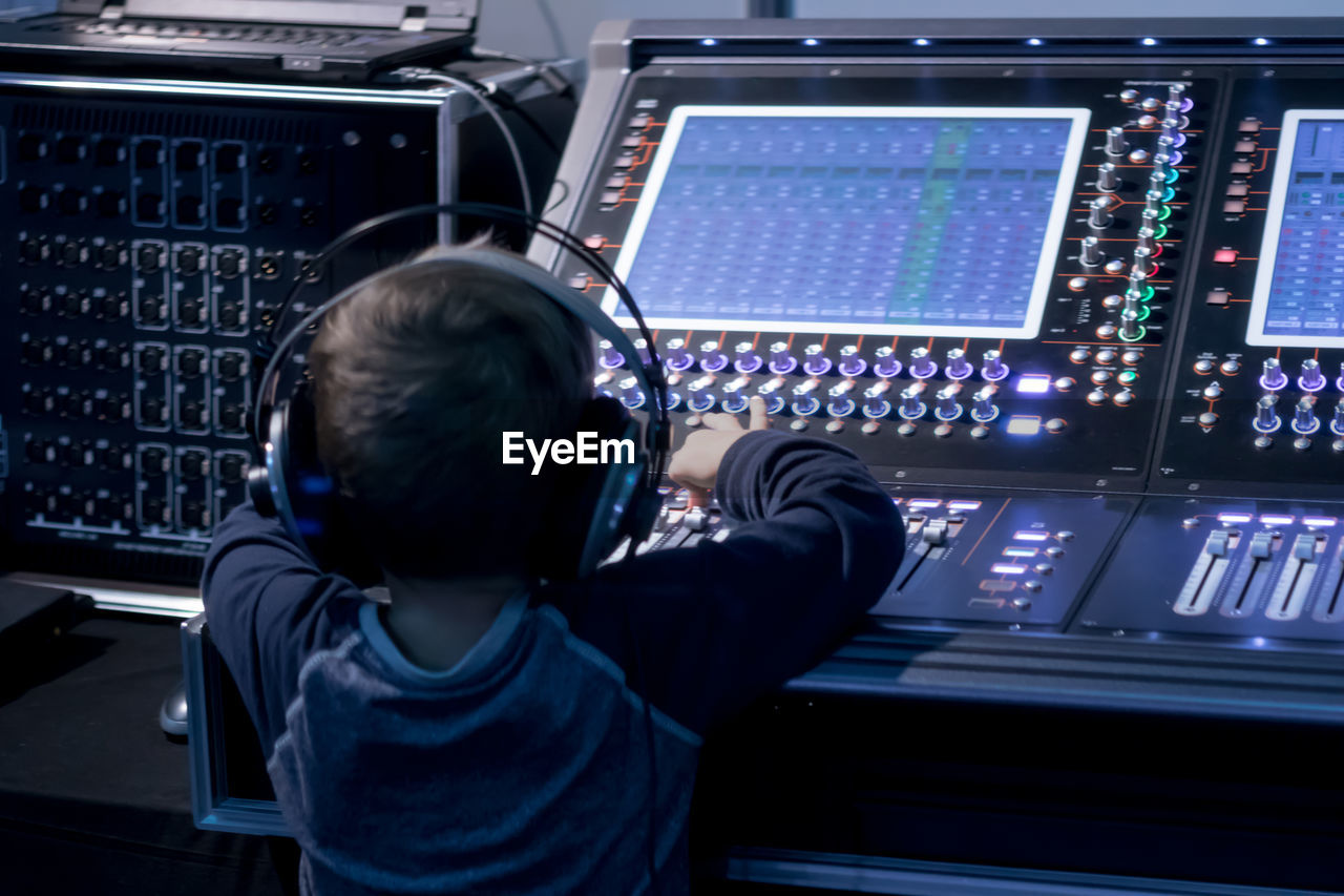 Rear view of boy using sound mixer in studio