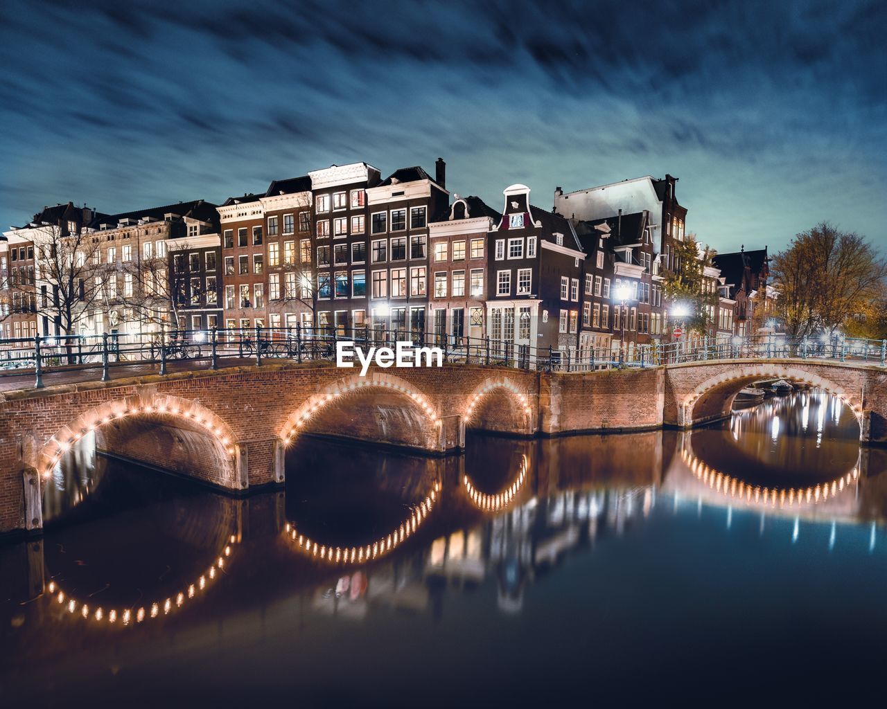 Illuminated bridge over river in city against sky at night