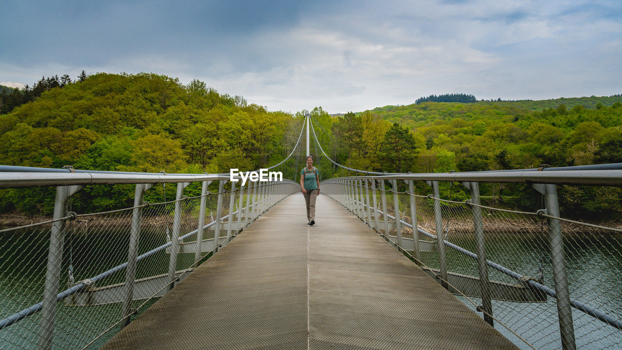 rear view of man walking on bridge against sky