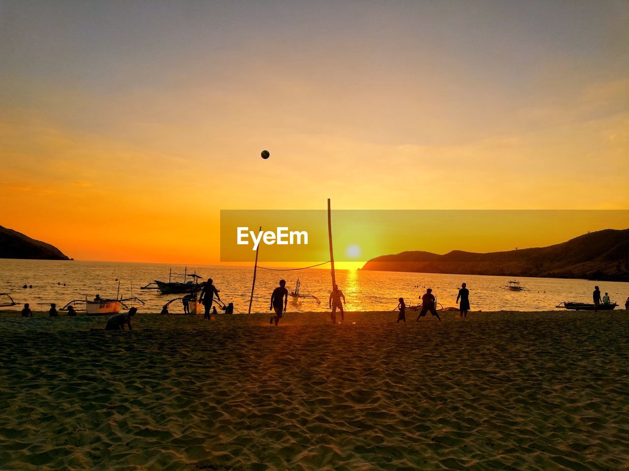 Silhouette of people playing beach volleyball against sky during sunset