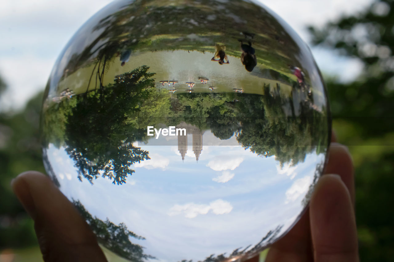 Cropped hand holding crystal ball with reflection of sky and trees