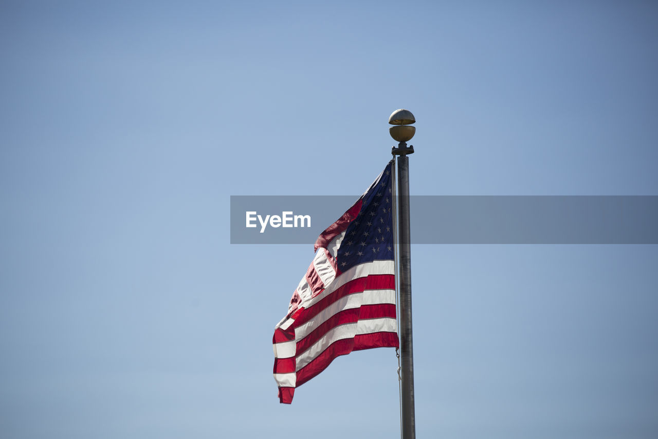 Low angle view of american flag waving against clear blue sky