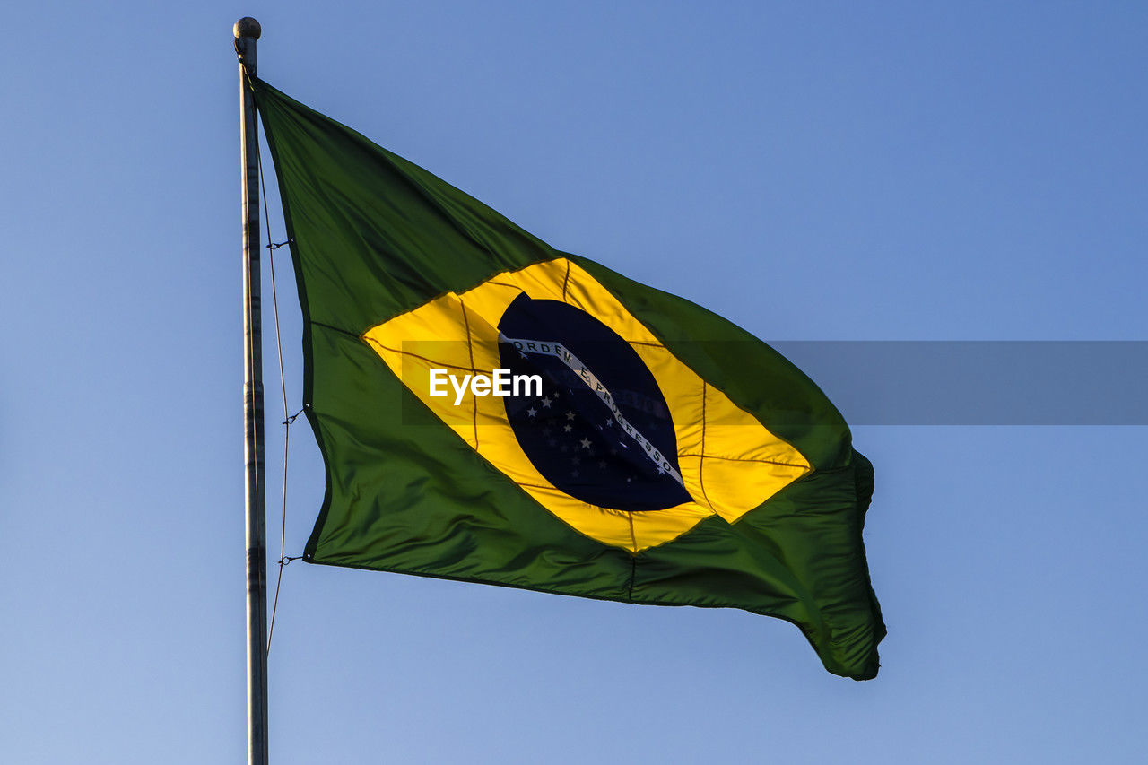 Brazilian flag flutters on a flagpole with the blue sky in the background