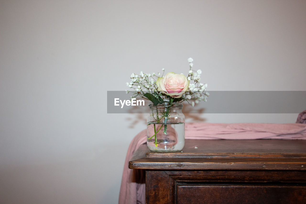 Close-up of flower vase on wooden table against wall