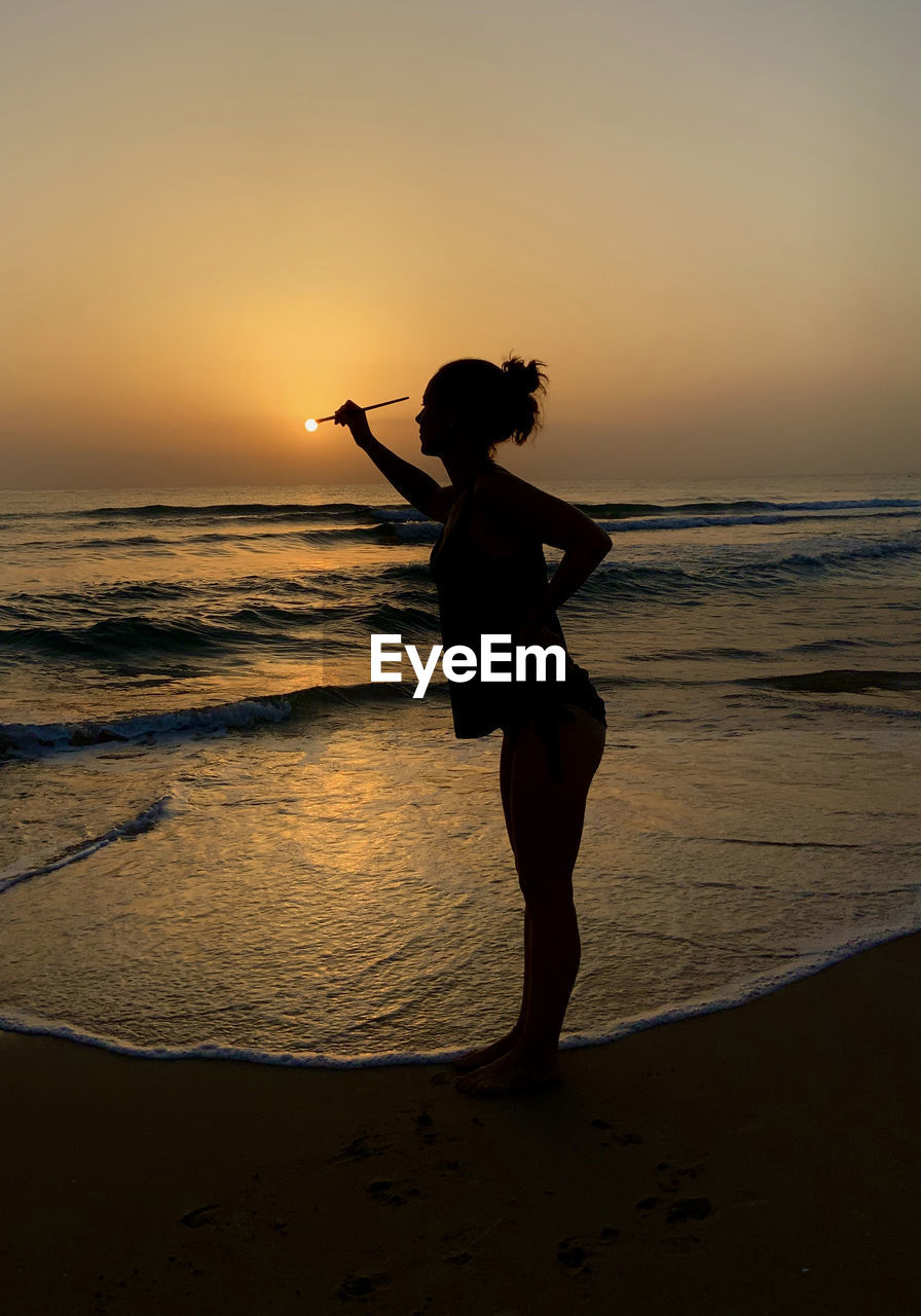 Full length of woman standing at beach during sunset