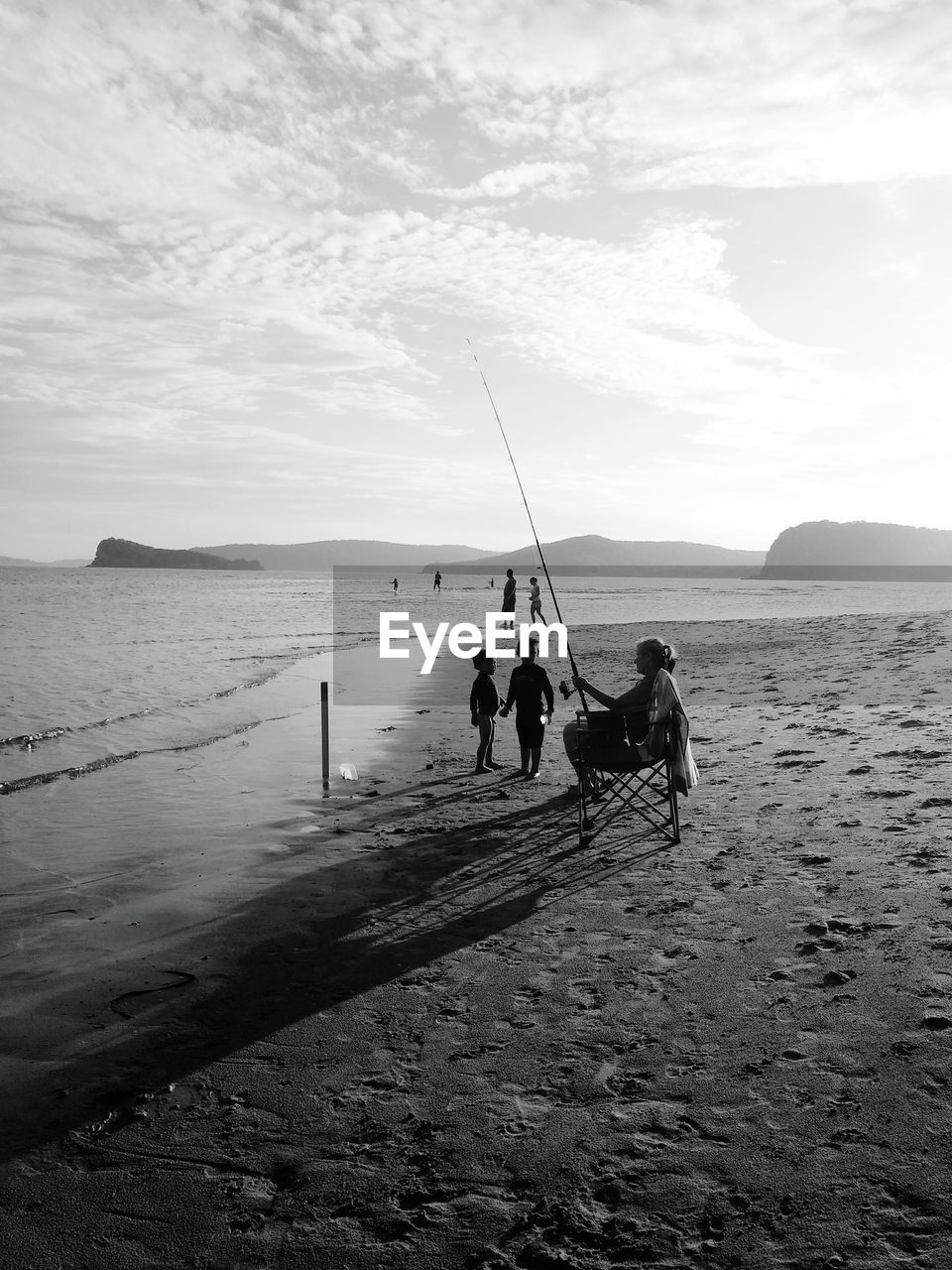 Children looking at woman fishing on beach