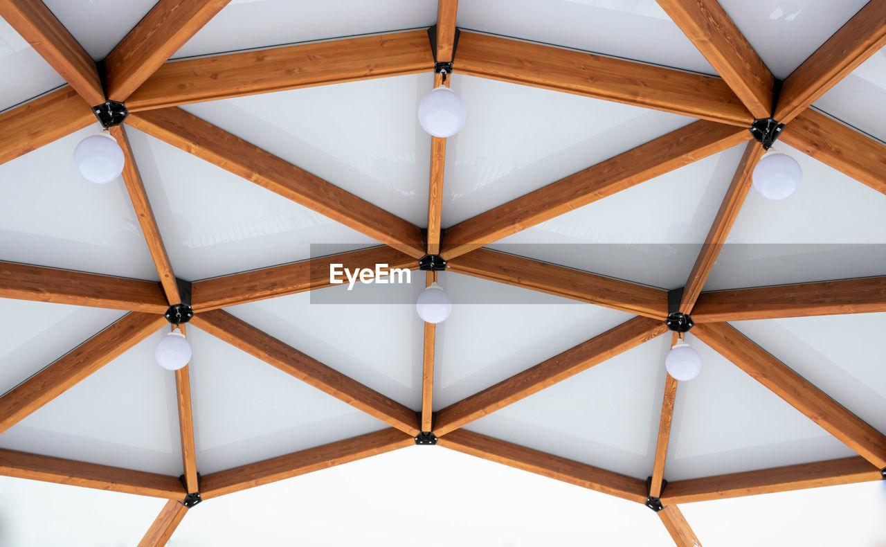 Glass ceiling with lanterns in a brown wooden gazebo outdoors in winter.