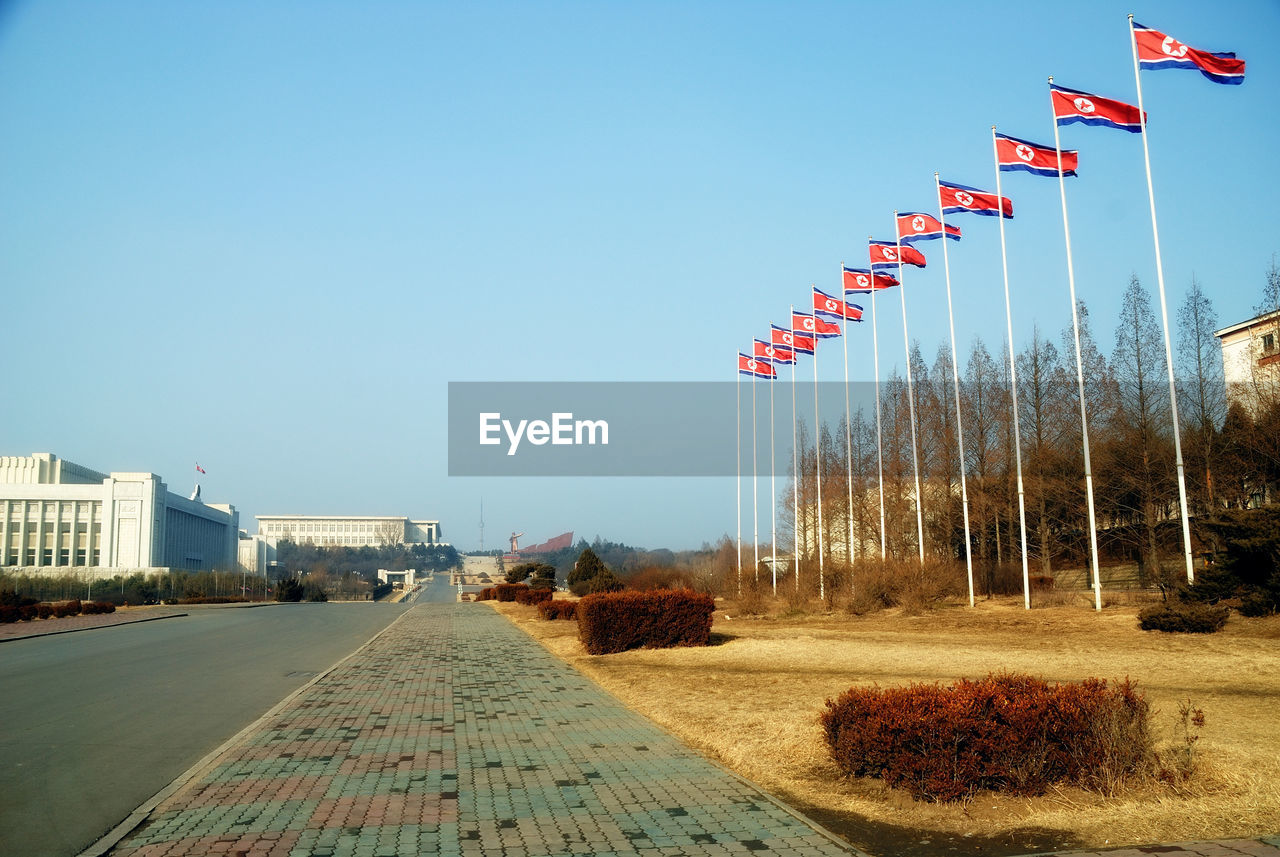 LOW ANGLE VIEW OF FLAGS AGAINST CLEAR BLUE SKY IN CITY