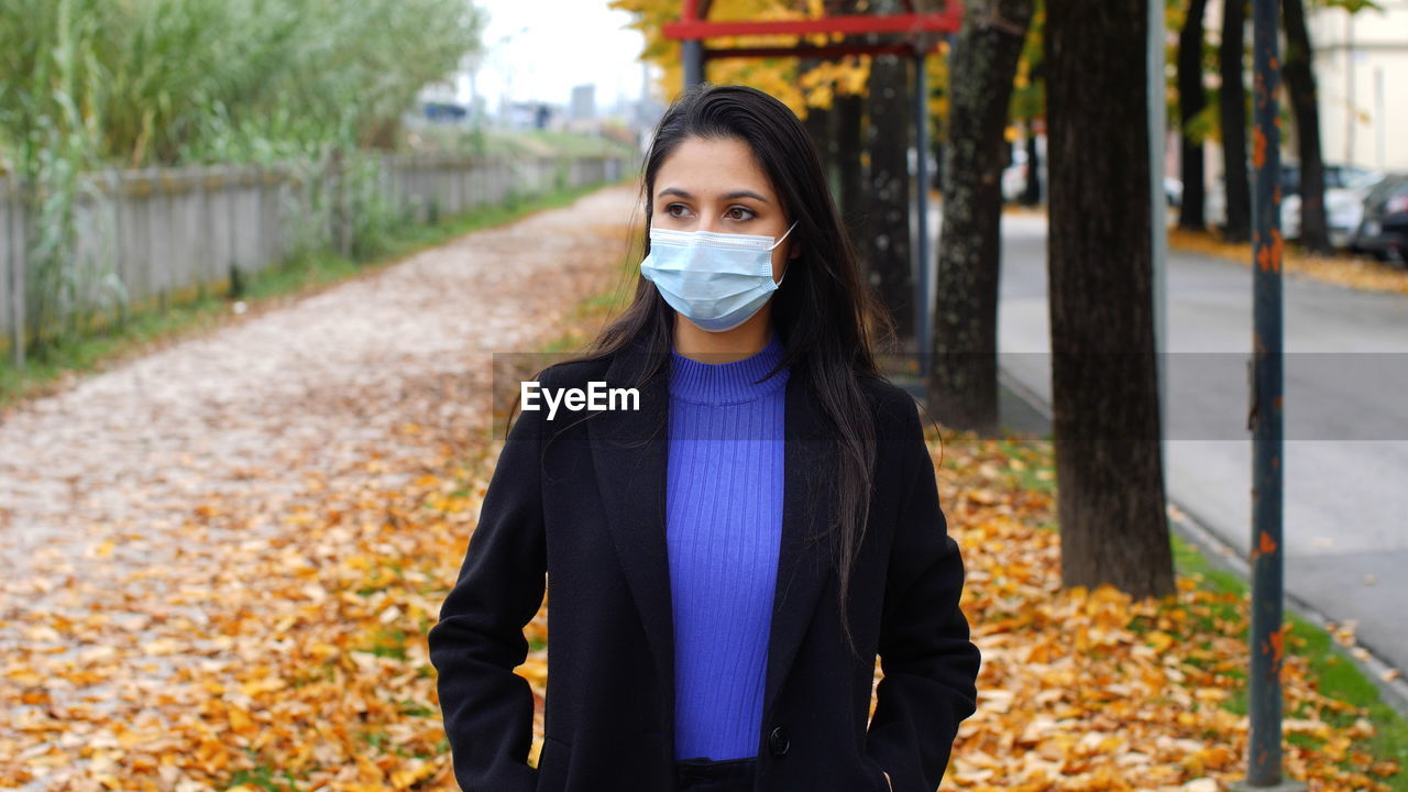 A young woman wears a surgical mask in the time of the covid-19 pandemic. autumn scenery.