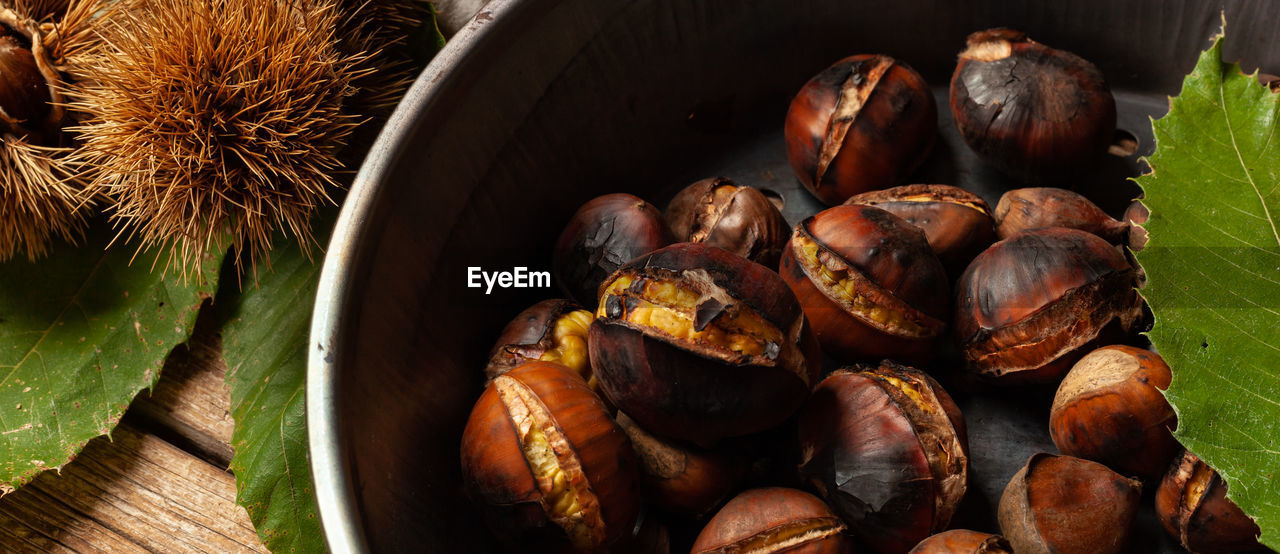 Roasted chestnuts in an iron skillet on a wooden table.