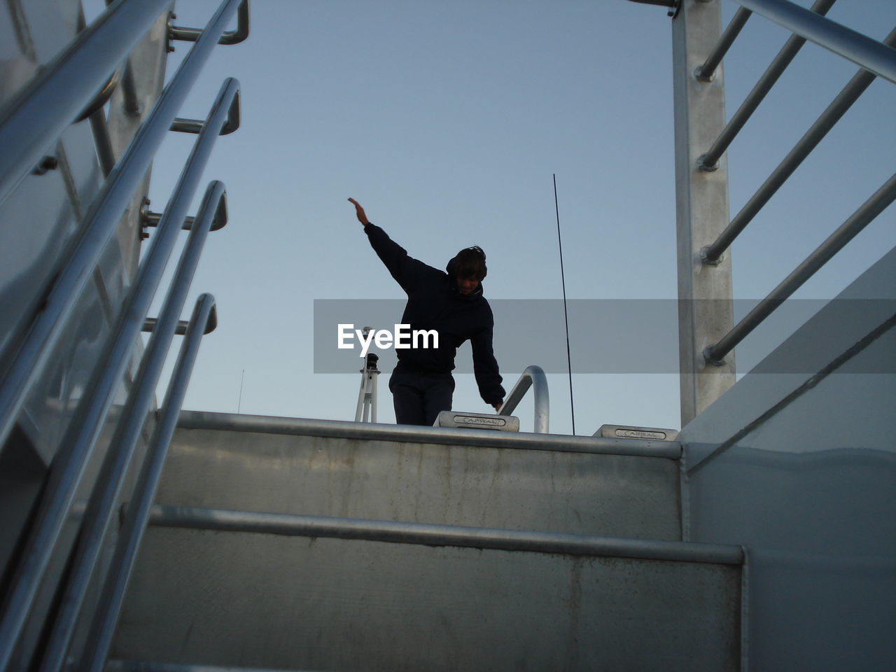 Low angle view of man with hand raised seen through steps against clear sky