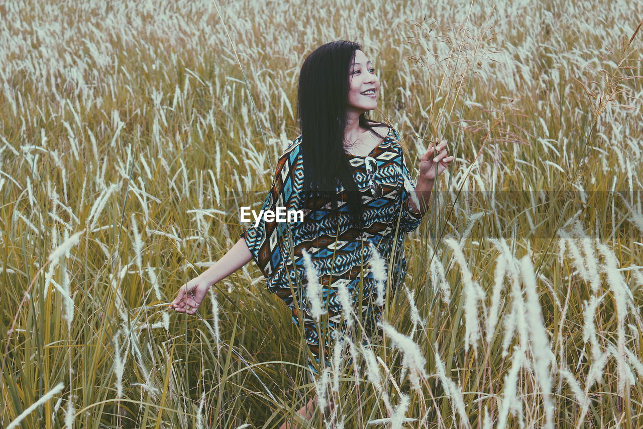 Young woman looking away while standing amidst plants on field