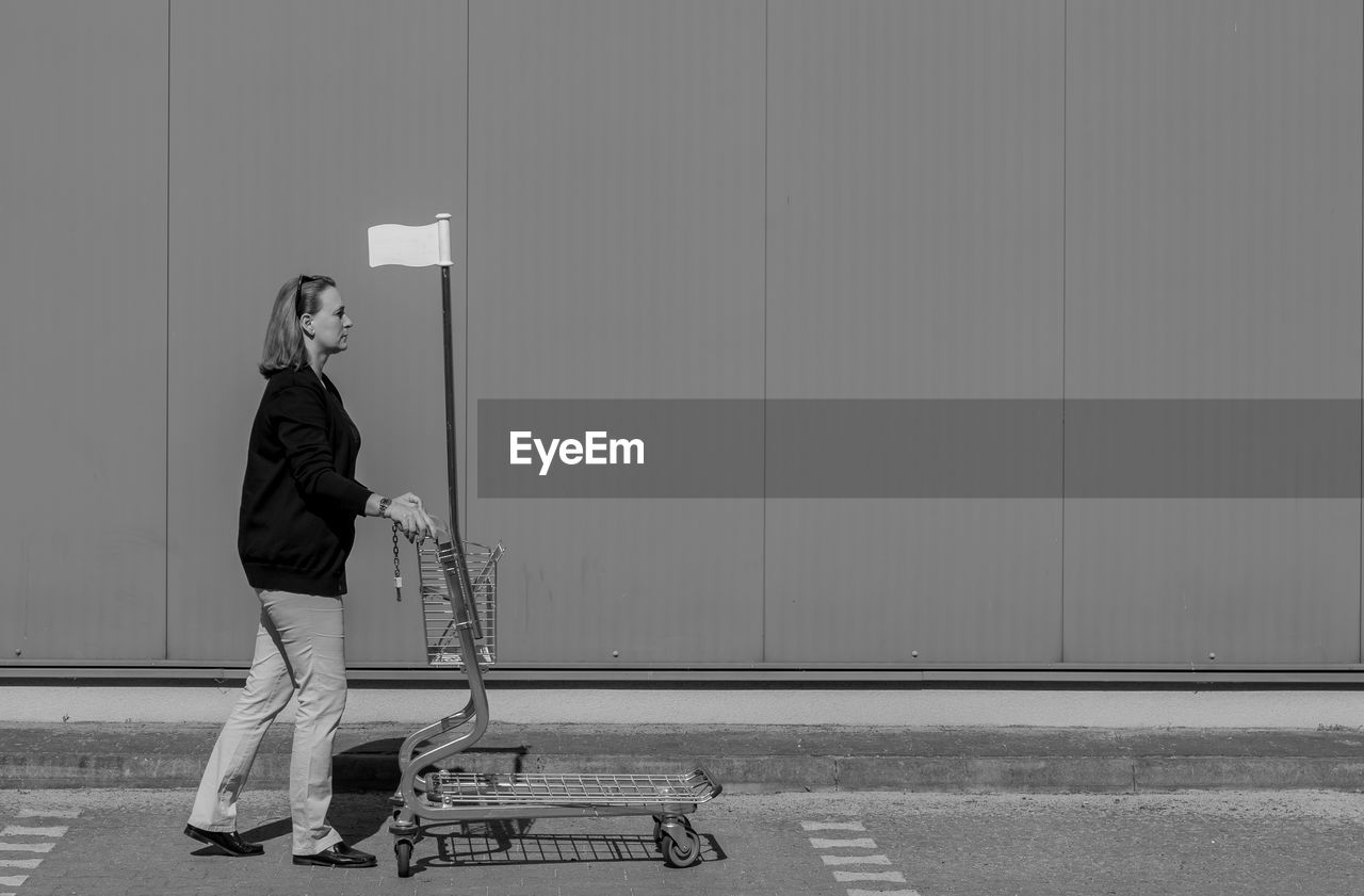 Woman with shopping cart against wall