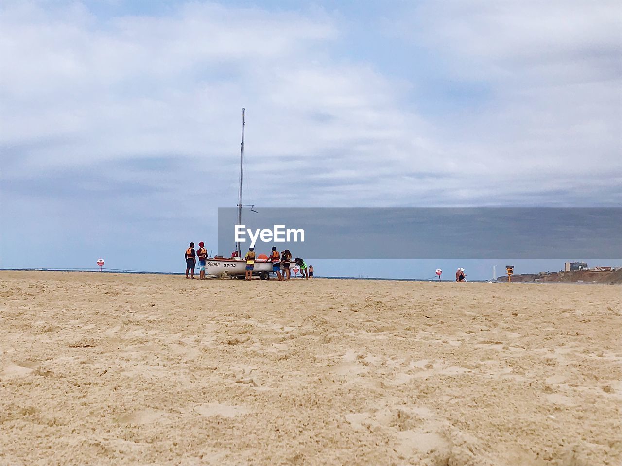 People with boat at beach against sky