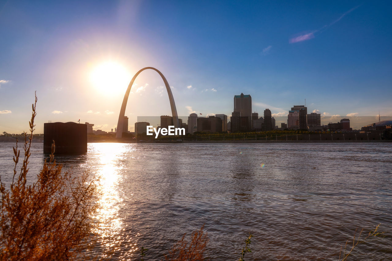 Scenic view of river by buildings against sky during sunset