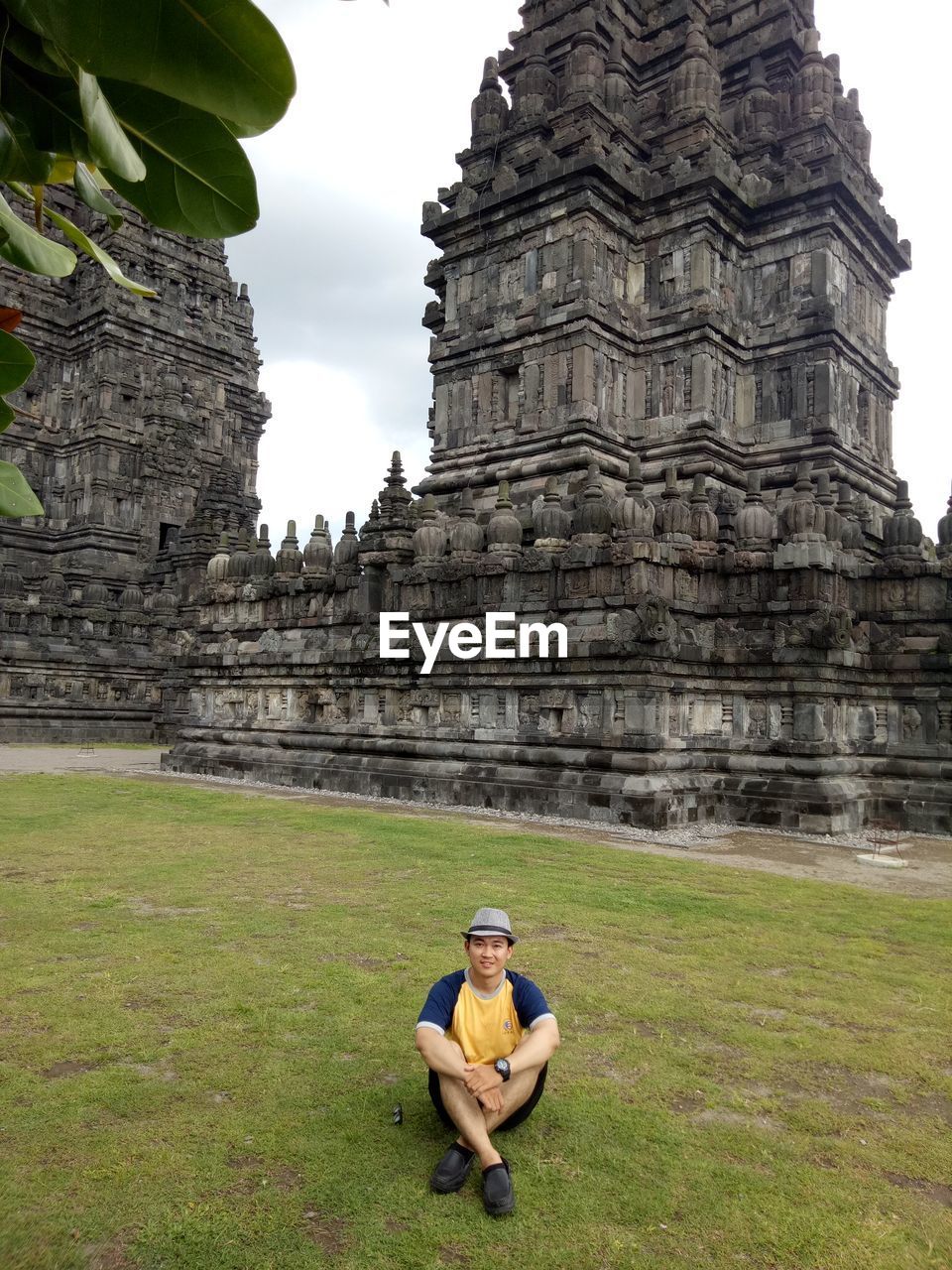 Portrait of young man sitting on grassy field against temple