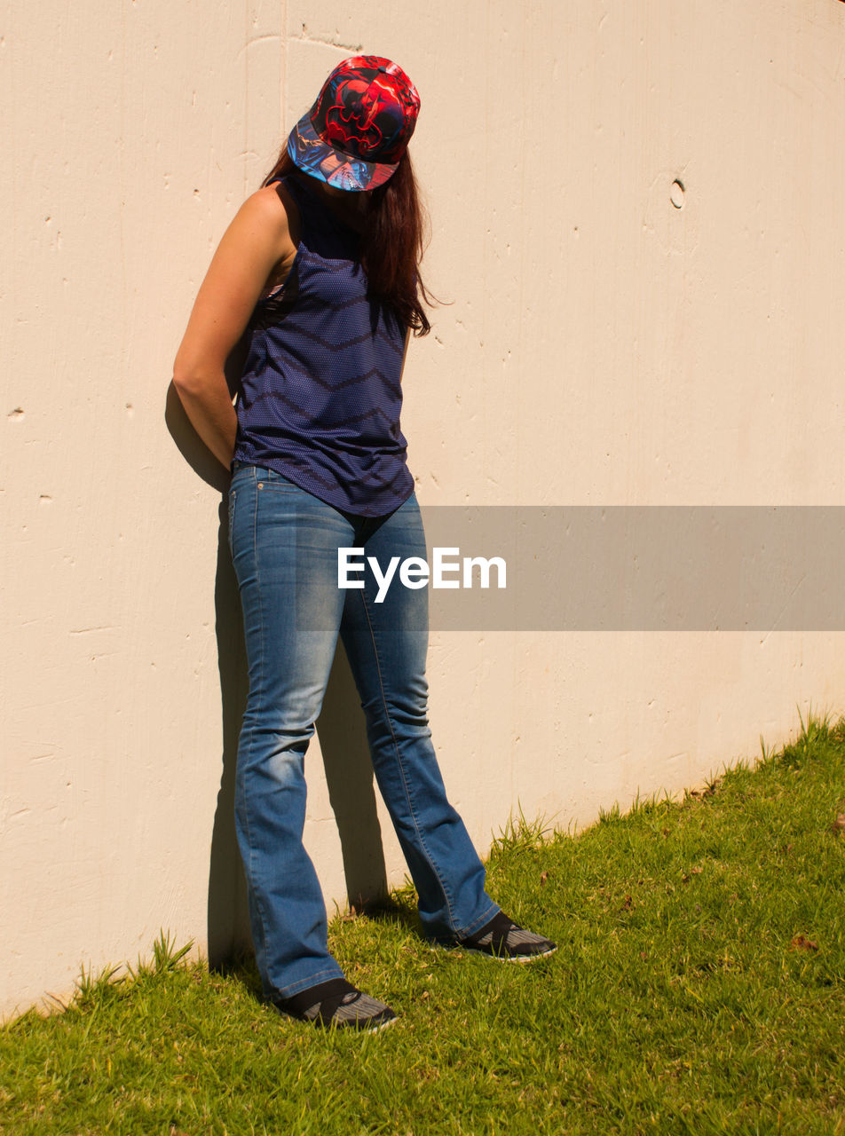 YOUNG WOMAN STANDING AGAINST WALL