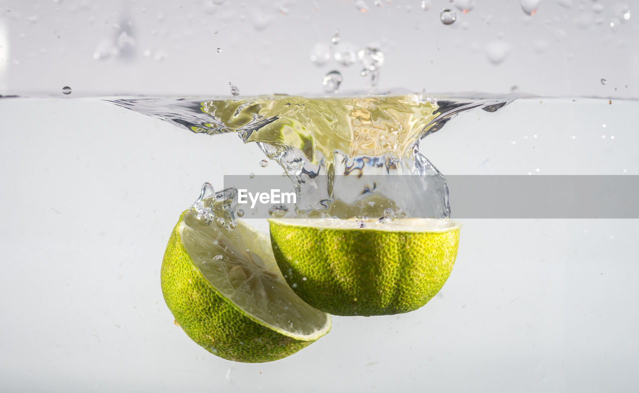 Close-up of limes fruit drop into water against white background