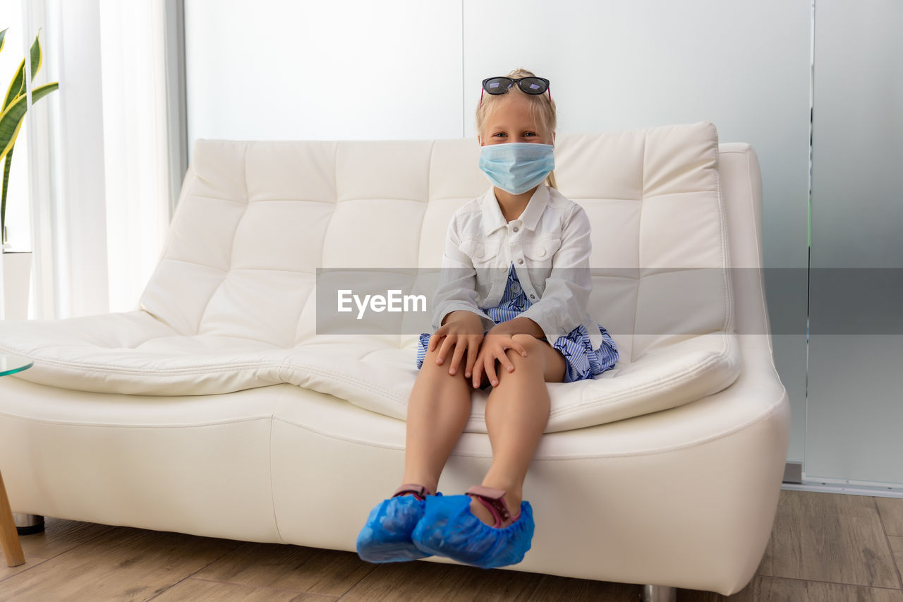 Portrait of girl with protective face mask sitting on sofa