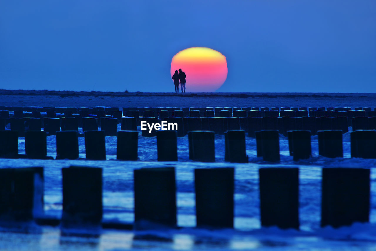 Silhouette couple on pier by sea against clear sky during sunset