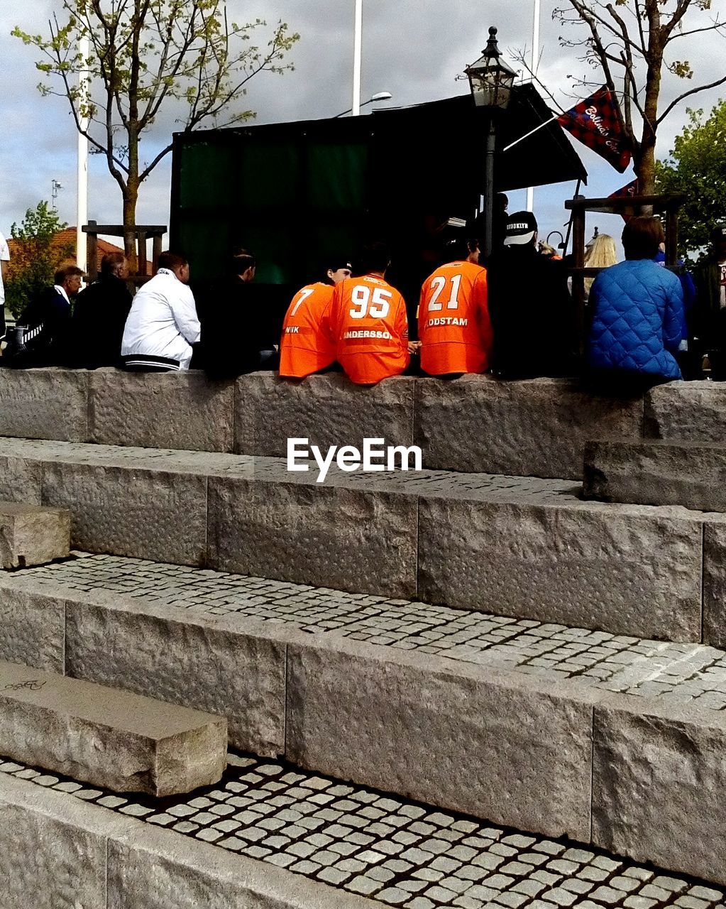 Rear view of people sitting on steps against cloudy sky